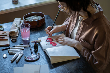 Freelance artist drawing sketch in art school, workshop, during master class. Cartoon animator creating animation painting. Artist tools, acrylic paints, pencils, rubber, sketch book lying on table