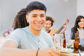 Young latin man, holding glass, looks at camera and enjoys the music played by his friends
