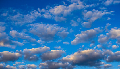 A vibrant blue sky dotted with dense, voluminous clouds. Dramatic lighting highlights the textures...