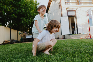 Two playful boys enjoying a sunny day in the backyard, one riding on the back of another, creating...