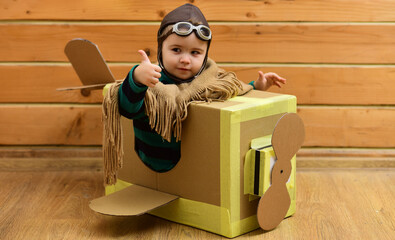 Flying child flying with cardboard wings. Kid dreams of pilot. Baby fly with paper plane. Boy in aviator helmet indoors. Child flying with toy airplane. Dreaming kid Flying in cardboard box.