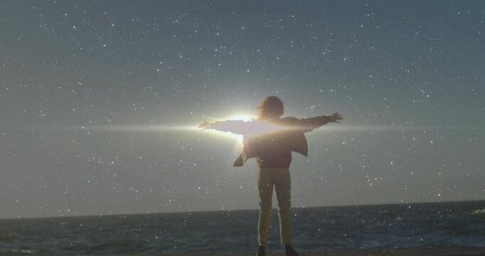 Woman raising arms and witnessing horizon glow becoming light flare behind barrier in technology