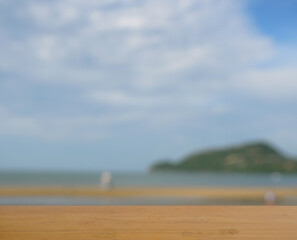 Empty brown wooden table surface for product placement with blur blue sea with sky with white cloud and brown beach in background