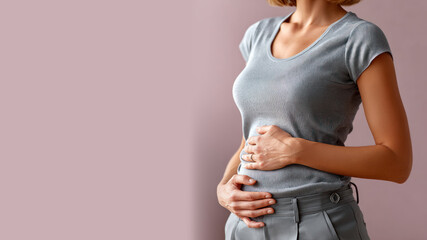 A woman holds her stomach which hurts due to menstrual problems isolated on pastel background