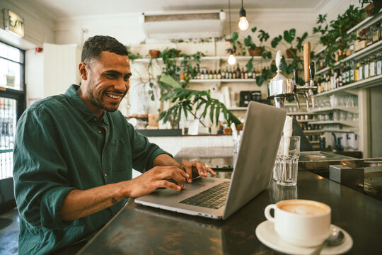 Smiling freelancer using laptop in cafe during daytime while working remotely