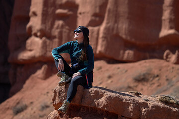 Young woman in sunglasses, female tourist sitting on sandstone cliff in canyon