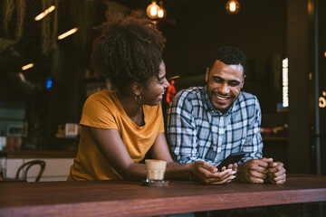 Cheerful young couple using smartphone and enjoying coffee in modern cafe