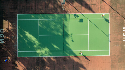Obraz premium Aerial View of a Tennis Court Game in Progress at UGM, Shadows Dancing on Green Surface