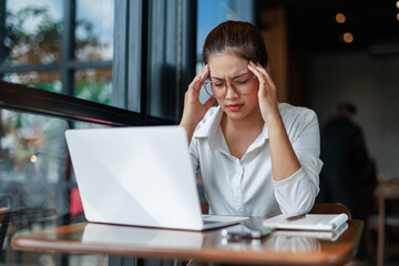 Young Asian businesswoman suffering from headache while working on laptop in cafe, touching temples...