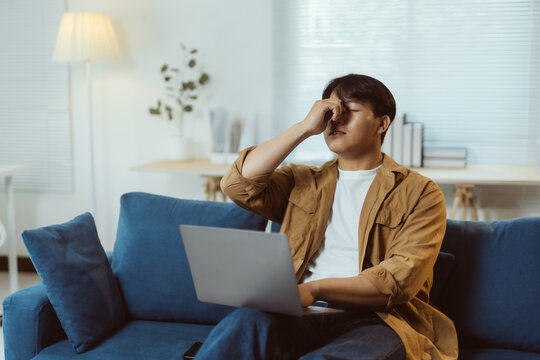 Young man rubbing his nose and eyes, suffering from eye strain, dry eye syndrome, tired from overwork, taking break from work on laptop