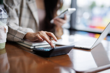 Businesswoman managing budget and investments while using a calculator and laptop in a modern office setting, focused on financial analysis