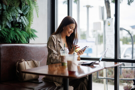 Young asian businesswoman holding credit card and using smartphone for online shopping while sitting in cafe