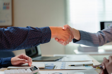 Business partners shaking hands after signing a contract at office desk, making a successful deal