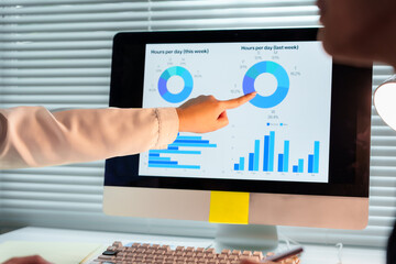 Obraz premium Two businesswomen pointing at computer screen showing financial charts and pie graphs, analyzing data and discussing work in office
