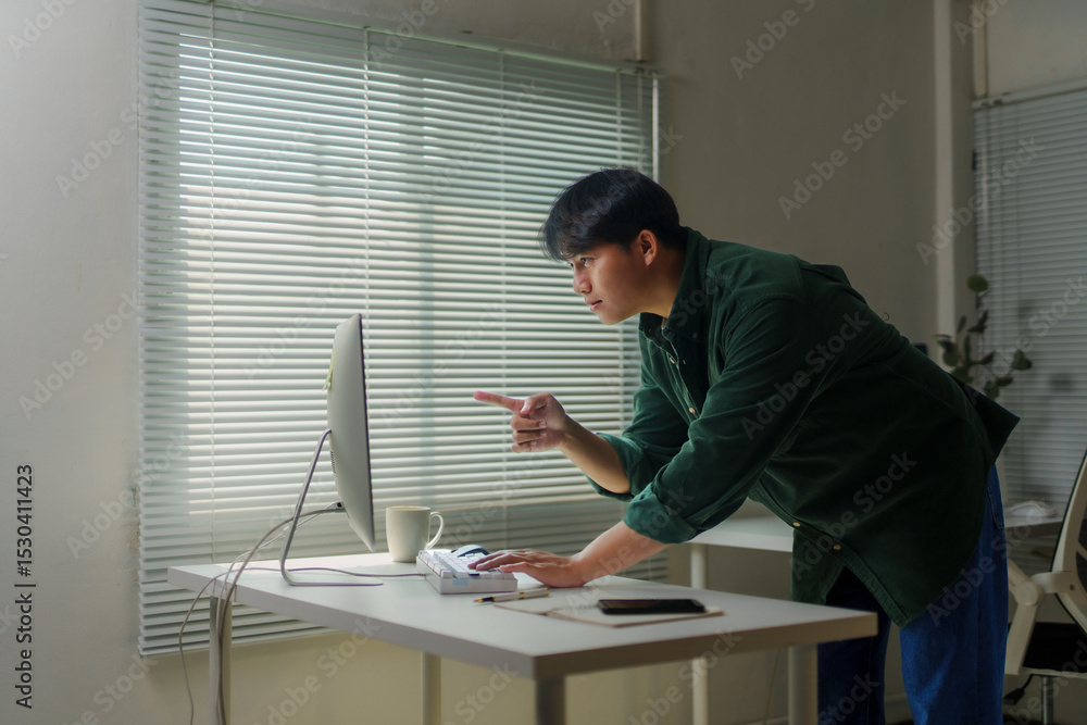 Poster young asian man focused on pointing at a computer screen while working remotely from a comfortable h