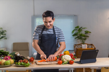 Young cook preparing a healthy meal at home, slicing carrots on a wooden cutting board, following...