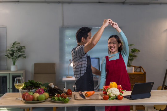 Happy asian couple dancing in the kitchen while preparing healthy food, recording a video tutorial