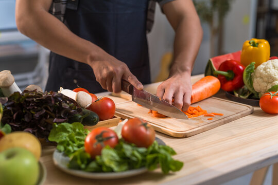 Chef using knife to slice carrots on cutting board, surrounded by various fresh vegetables, promoting healthy eating and culinary skills