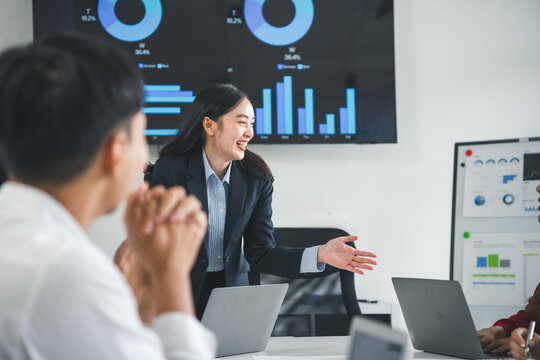 Asian businesswoman leading meeting discussing work with team using laptop computer and digital tablet present financial chart on monitor screen