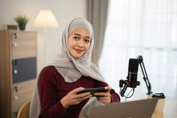 Young woman in hijab engaging in content creation while holding smartphone in modern workspace,...