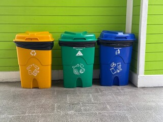 Three colorful recycling bins for waste separation against a green wall, ideal for environmental...