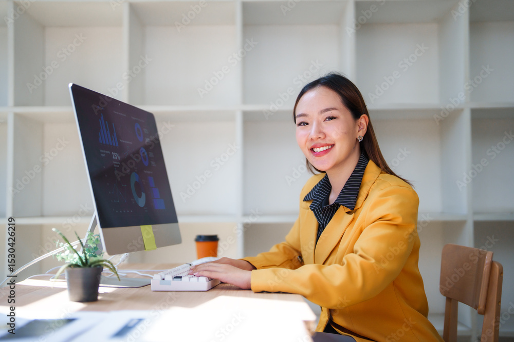 Aufkleber young asian businesswoman smiling and working with computer analyzing charts and graphs on screen in