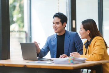 Two businesspeople engaging in a lively discussion while collaborating over a laptop in a bright, modern office setting