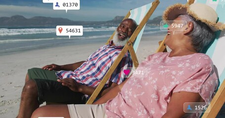 Senior couple relaxing on beach chairs, tapping phone and viewing floating social media metrics - Powered by Adobe