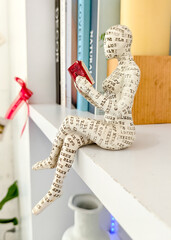 Bookworm Sculpture: A unique, artistic sculpture of a person engrossed in reading a book sits on a shelf, capturing the essence of leisure and the joy of reading.