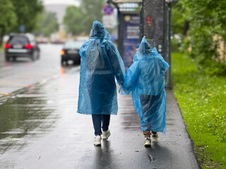 A woman and her daughter are walking around the city in rainy weather in blue transparent raincoats. She has the hood of the coat on. People in a blue raincoat in the rain. Family trip. Bad weather. 