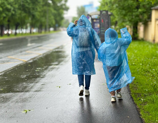A woman and her daughter are walking around the city in rainy weather in blue transparent...
