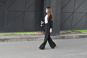 Woman walking in stylish outfit holding sunglasses near modern geometric wall.