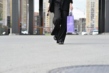 Woman holding a purple shopping bag while standing on a street in a residential area.