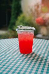 Drink in cafe. Refreshing Bright Red Drink in a Clear Plastic Cup on a Green and White Checkered Tablecloth