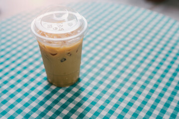Drink in cafe. Iced coffee in a clear cup on a checkered tablecloth, showcasing a refreshing summer beverage for warm days and outdoor relaxation