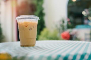 Drink in cafe. Refreshing Iced Coffee in Clear Plastic Cup on Café Table Outdoors with Greenery and Flowers in Background