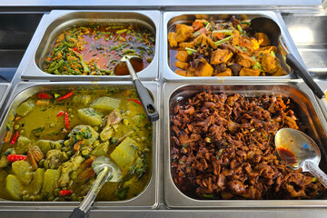 A colorful selection of Thai street food curries and stir-fried dishes served in stainless steel trays at a local mixed rice vendor.