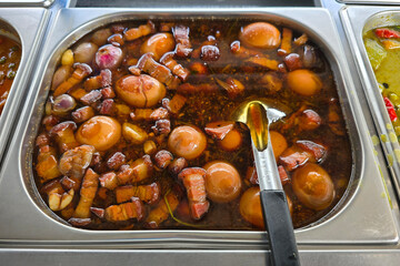 A rich and flavorful braised pork dish simmered in soy sauce, served with boiled eggs and garlic cloves in a stainless steel tray.
