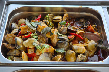 A flavorful tray of stir-fried clams with chili, basil leaves, and savory sauce, served hot in a mixed rice setting.