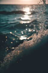A powerful close-up of a foamy wave cresting with golden sun flare sparkling in the background over the ocean surface during a warm evening light, with copy space.