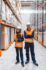 Logistics workers standing between shelves in warehouse, holding barcode scanner and digital tablet, managing inventory