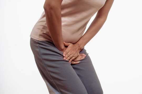 Confident young Asian woman in light brown shirt stands against a white background, experiencing vaginal pain. inflammation, cysts, endometriosis gynecological conditions affecting female health.