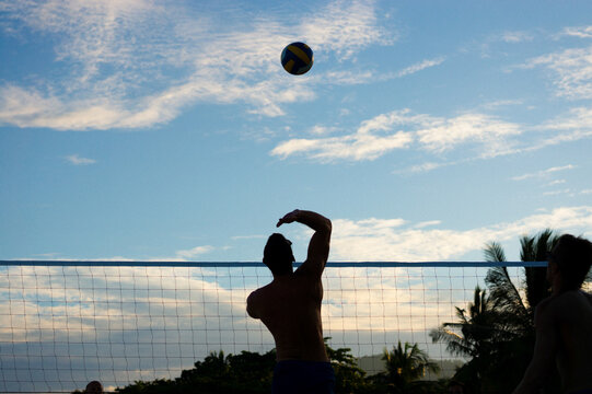 Man jumping to hit volleyball on outdoor court at sunset