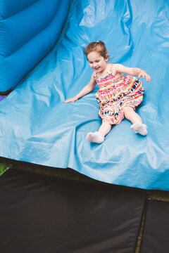 Toddler girl sliding on a bouncy castle, summer holiday
