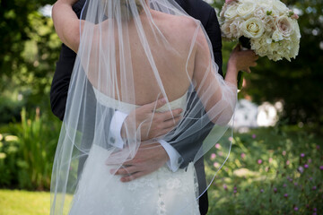 Bride and Groom Embrace Under Veil with Bridal Bouquet