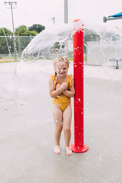 Child smiling under fountain at urban splash pad during summertime