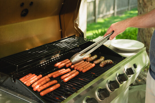 Person grilling hot dogs and sausages on an outdoor barbecue - Powered by Adobe