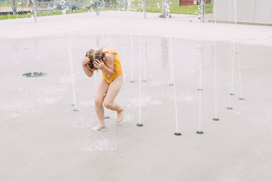 Young girl running through splash pad fountains