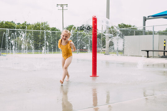 Giggling child running through splash pad sprinkler at city park