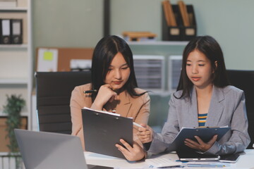 Two young Asian business woman talk, consult, discuss working with new startup project idea presentation analyze plan marketing and investment in the office.
